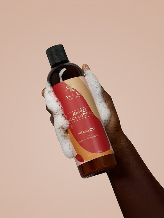 As I Am Jamaican Black Castor Oil Shampoo - imagen de retrato de la botella sostenida en la mano, mostrando la fórmula libre de sulfatos diseñada para limpiar, fortalecer y apoyar el crecimiento saludable del cabello con JBCO.