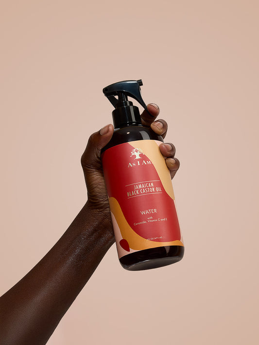 As I Am Jamaican Black Castor Oil Water - retrato de la botella de spray hidratante en la mano, destacando su fórmula ligera con JBCO para refrescar e hidratar los rizos naturales.