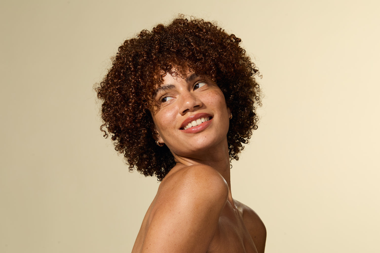 Mujer con el pelo rizado sonriendo sobre un fondo beige