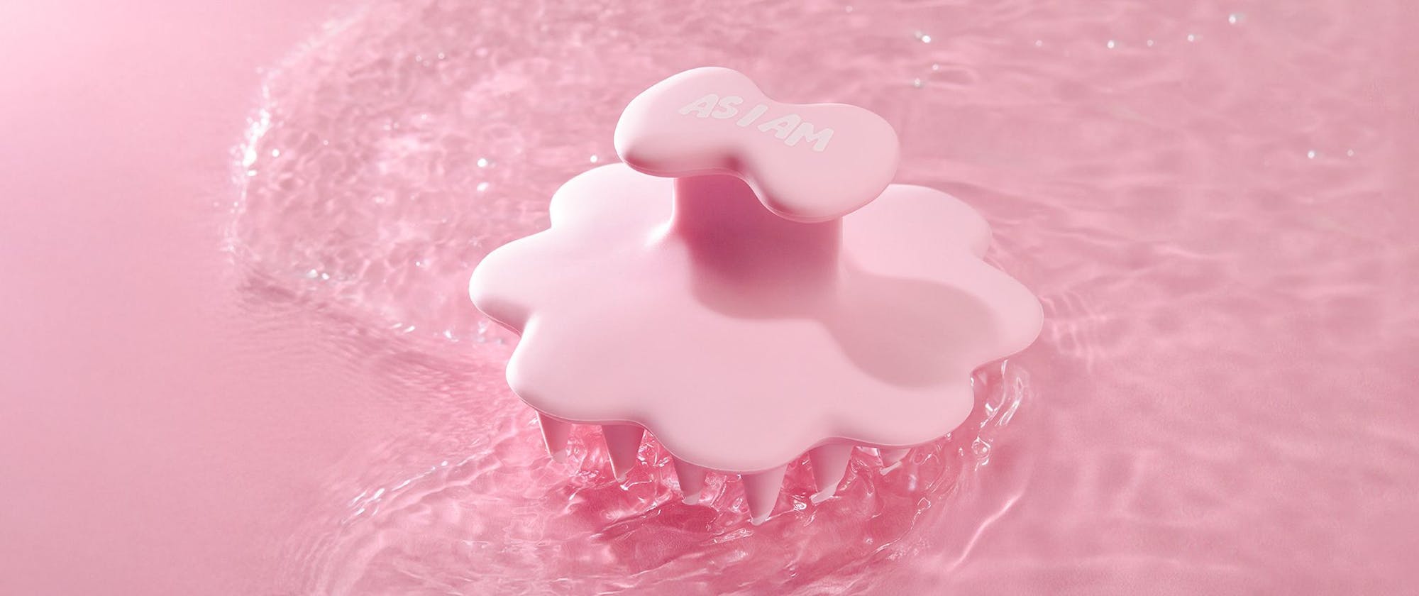 Cepillo para el cuero cabelludo con gotas de agua sobre fondo rosa
