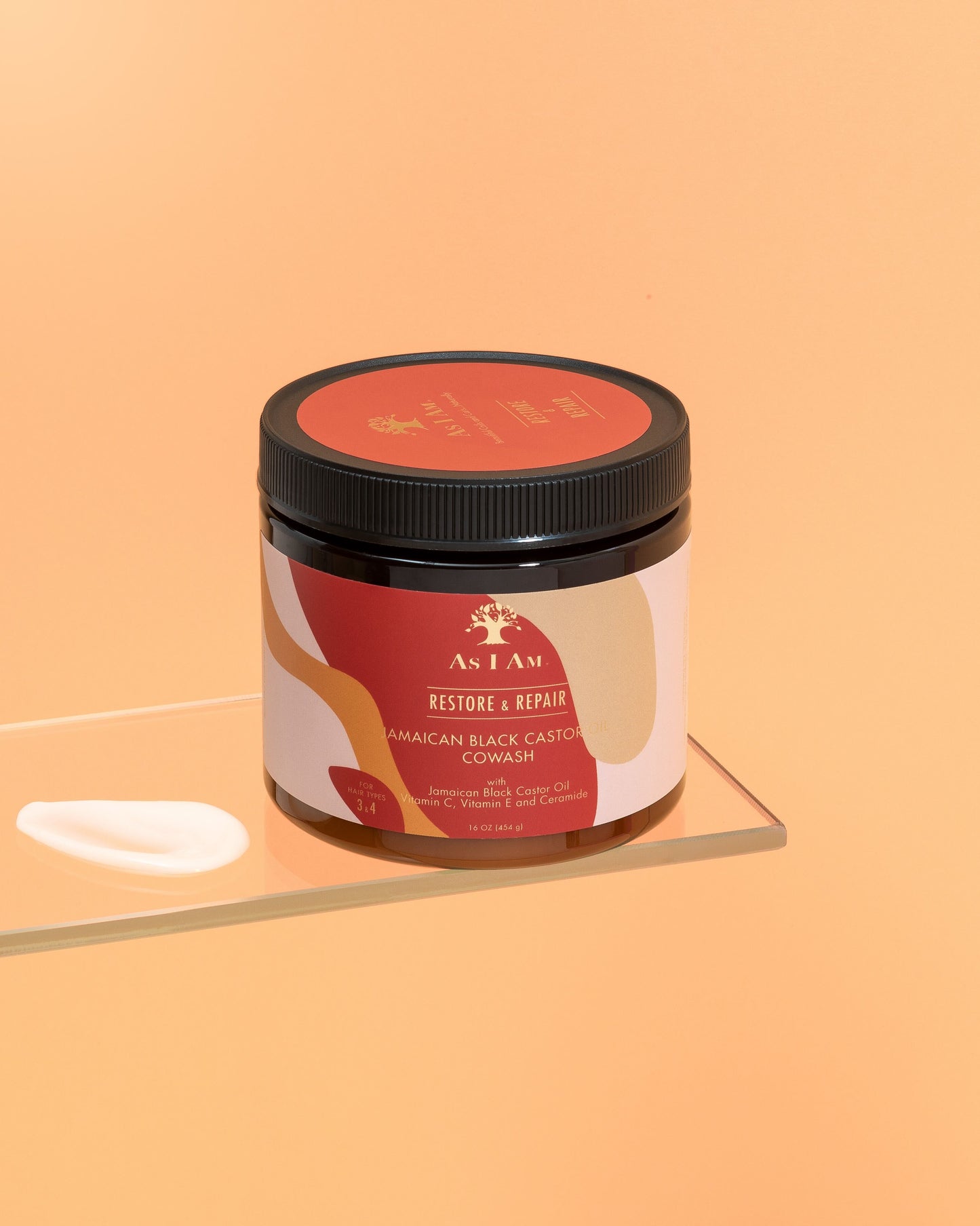 Un envase de aceite de ricino negro jamaicano Cowash con una etiqueta que muestra los detalles del producto, colocado sobre una superficie reflectante con un fondo naranja sólido.