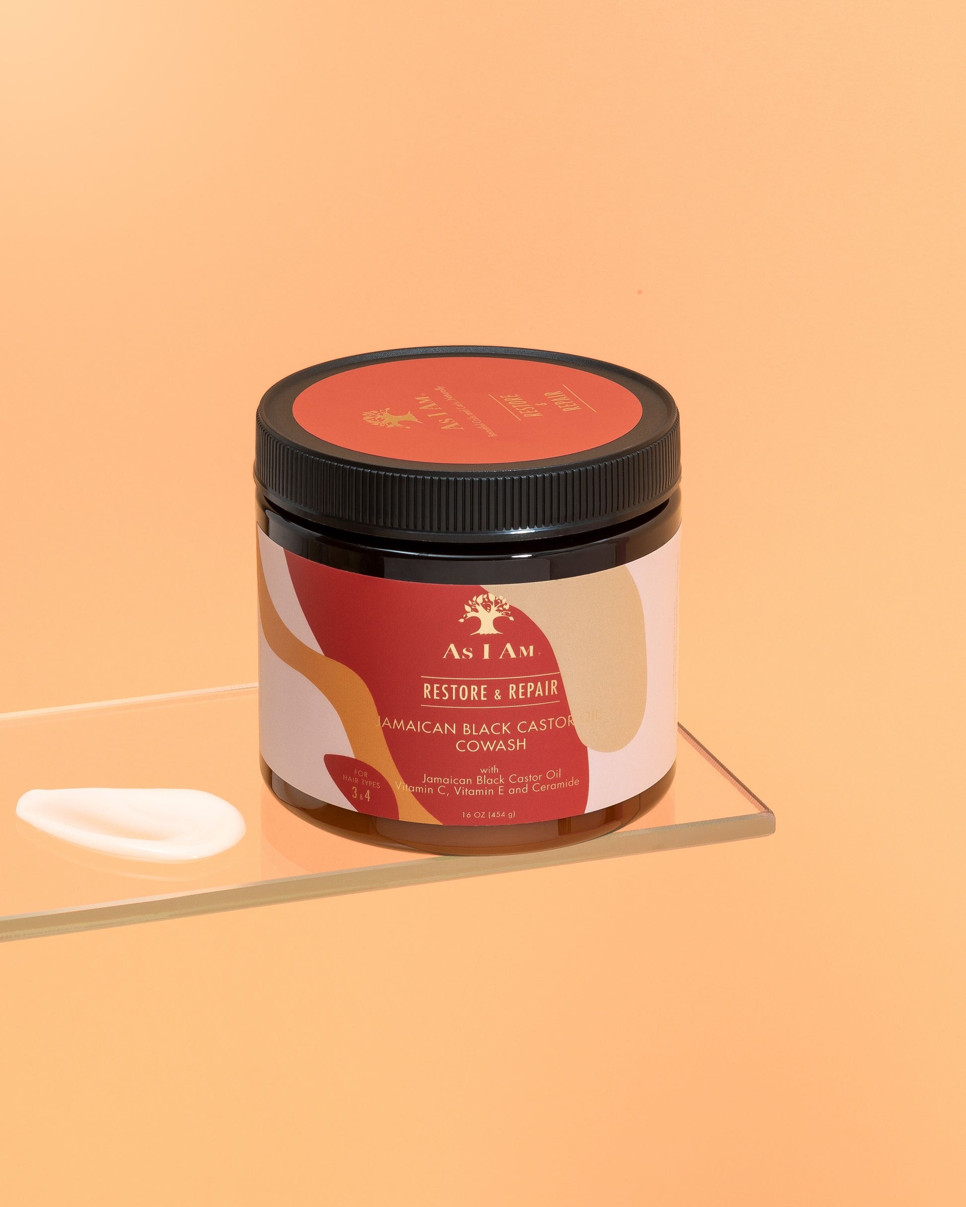 Un envase de aceite de ricino negro jamaicano Cowash con una etiqueta que muestra los detalles del producto, colocado sobre una superficie reflectante con un fondo naranja sólido.