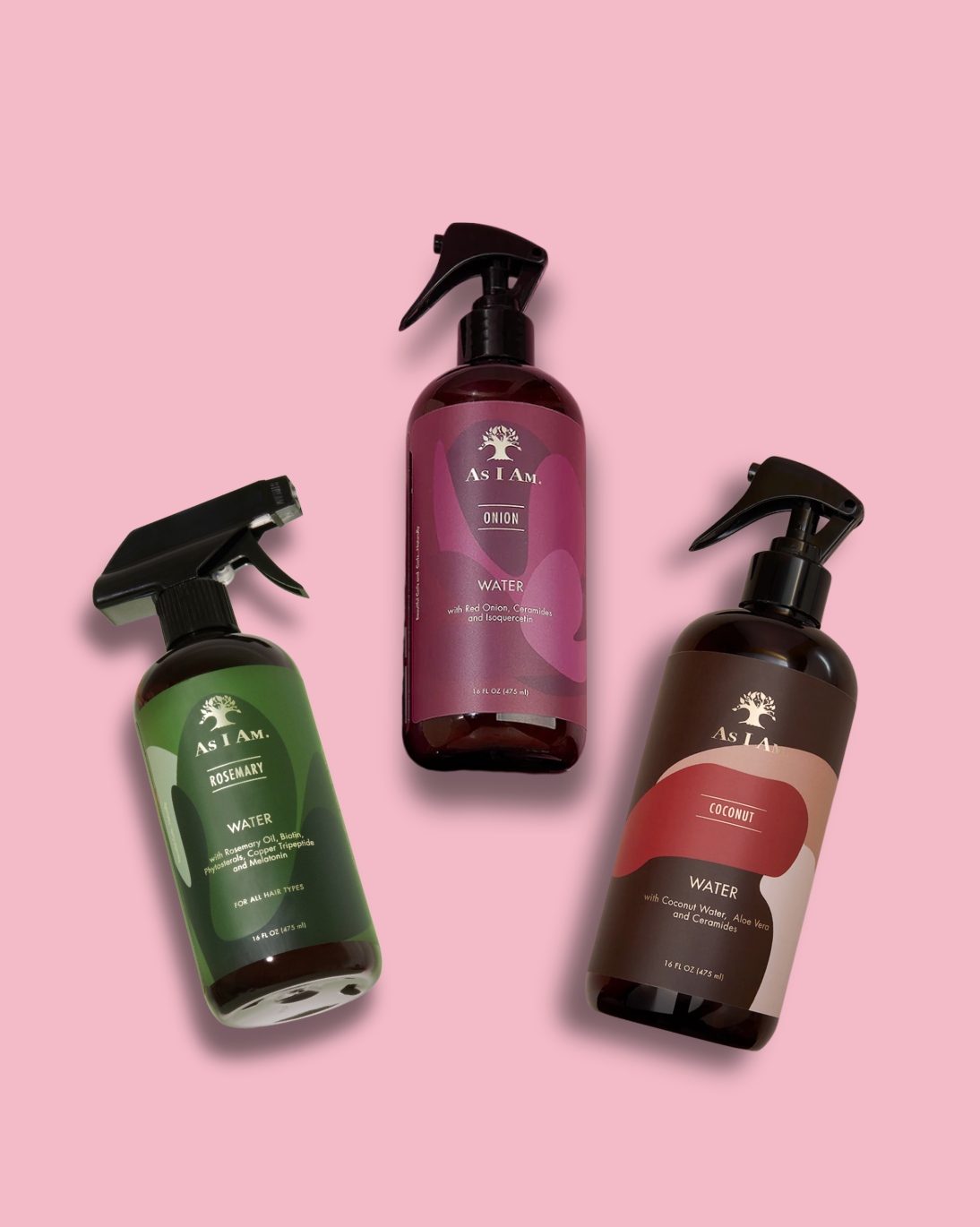 Tres botellas de productos para el cuidado del cabello As I Am sobre un fondo rosa.