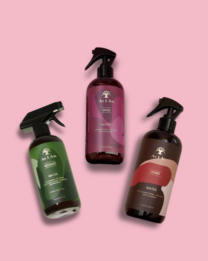 Tres botellas de productos para el cuidado del cabello As I Am sobre un fondo rosa.